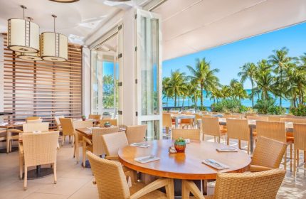 Hyatt Regency Waikiki Beach Resort's open-air restaurant. Tables with wicker chairs overlook palm trees and the ocean. Gay-friendly hotel dining.