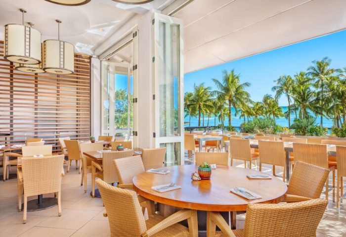 Hyatt Regency Waikiki Beach Resort's open-air restaurant. Tables with wicker chairs overlook palm trees and the ocean. Gay-friendly hotel dining.