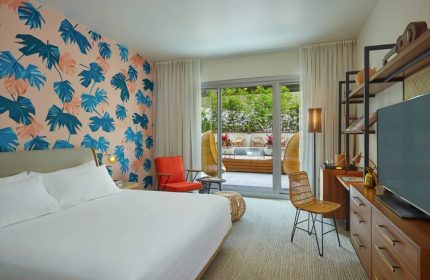 The Laylow Autograph Collection gay-friendly hotel room. Bedroom with tropical wallpaper, balcony, rattan chair. Ideal for gay travel.
