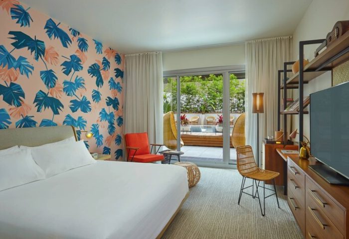 The Laylow Autograph Collection gay-friendly hotel room. Bedroom with tropical wallpaper, balcony, rattan chair. Ideal for gay travel.