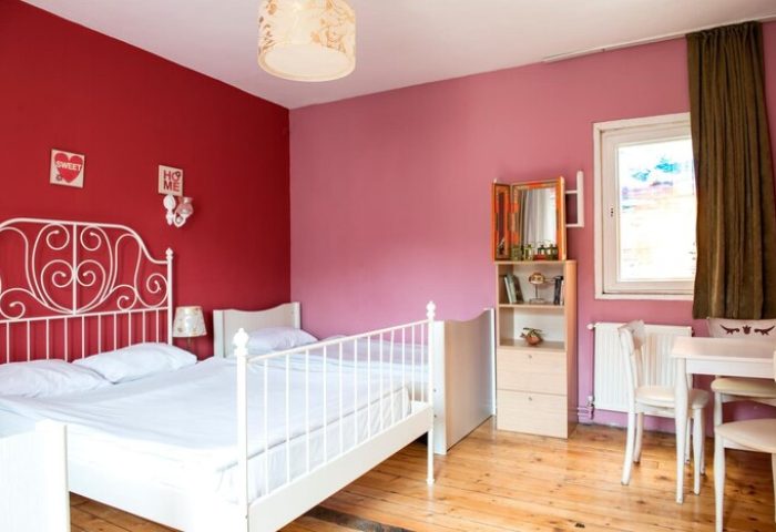 Cheers Midtown Hostel gay-friendly hotel room. White beds, red and pink walls, wood floors, desk, chair, and shelving unit.