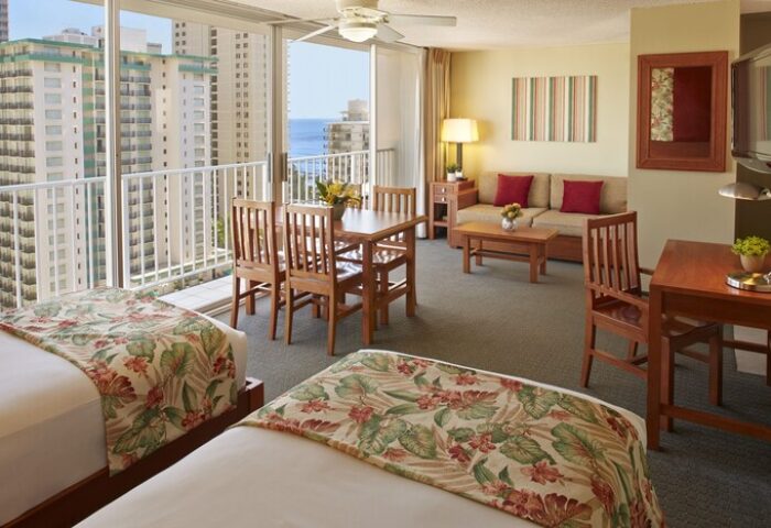 Pacific Monarch Hotel gay-friendly suite with ocean view. Two beds, dining table, sofa, and desk. Perfect for gay travelers seeking comfort.