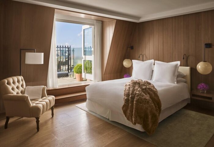 The London EDITION gay-friendly hotel room: wood paneled walls, a tufted chair, & balcony access. Perfect for gay travel in the city.