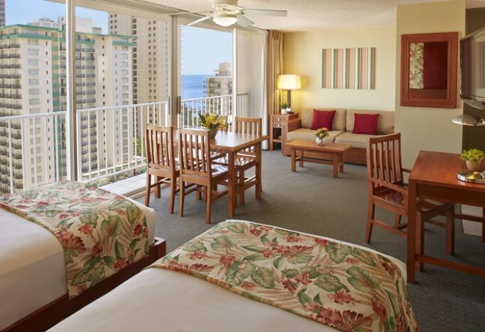 Pacific Monarch Hotel gay-friendly suite with ocean view. Two beds, dining table, sofa, and desk. Perfect for gay travelers seeking comfort.
