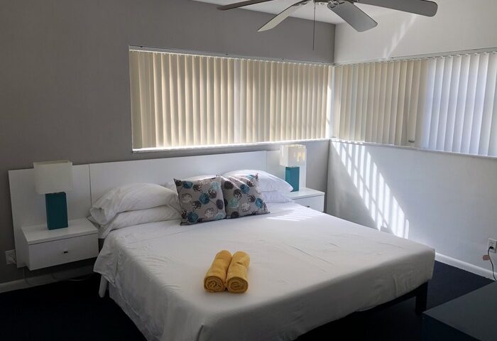 Cheston House gay-friendly hotel room. All-male guesthouse with a king bed, ceiling fan, & two windows with blinds. Yellow towels on bed.