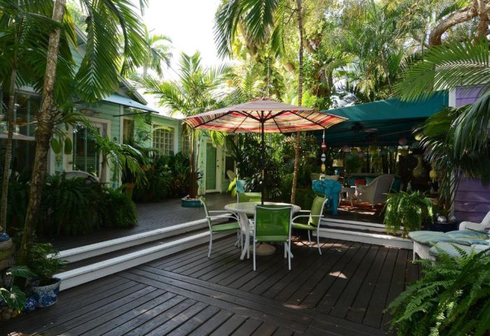 Pineapple Point Guesthouse, a gay men's resort. Outdoor deck with table, chairs, umbrella, and lush tropical landscaping. Gay-friendly hotel.