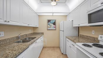 Coconut Bay Resort gay-friendly hotel kitchen. White cabinets, granite countertops, stainless steel sink, and appliances. Ceiling fan and fruit art.