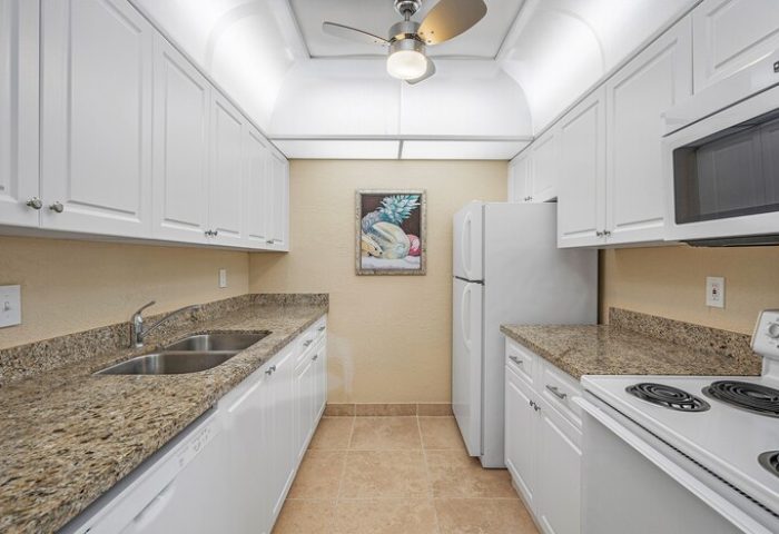 Coconut Bay Resort gay-friendly hotel kitchen. White cabinets, granite countertops, stainless steel sink, and appliances. Ceiling fan and fruit art.