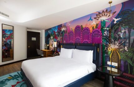 Hotel Indigo Dubai Downtown gay-friendly room. King bed with white linens, colorful mural, desk, mirror, and side table. Modern decor.
