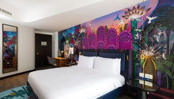 Hotel Indigo Dubai Downtown gay-friendly room. King bed with white linens, colorful mural, desk, mirror, and side table. Modern decor.