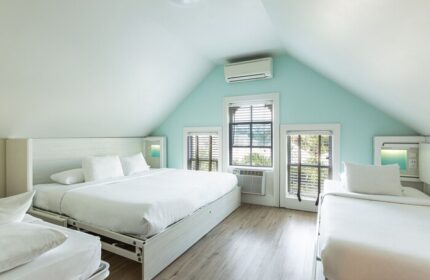 NYAH Key West adults-only, gay-friendly hotel room. Beds with white linens, windows with blinds, and light blue walls in a cozy, modern space.