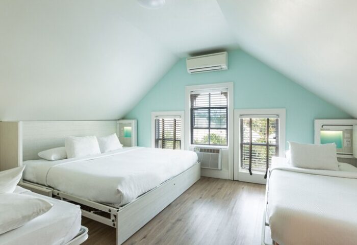 NYAH Key West adults-only, gay-friendly hotel room. Beds with white linens, windows with blinds, and light blue walls in a cozy, modern space.