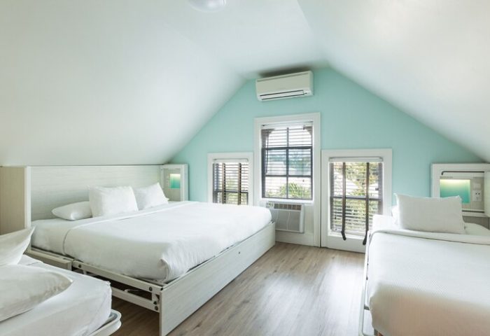 NYAH Key West adults-only, gay-friendly hotel room. Beds with white linens, windows with blinds, and light blue walls in a cozy, modern space.