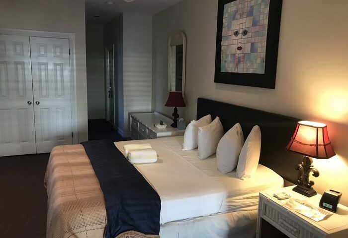 Bedroom interior at a gay-friendly hotel in New Orleans. Queen bed with white linens, bedside lamps, and unique wall art. Comfortable stay.