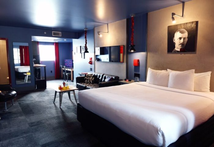 Hotel Gaythering, gay-friendly hotel. Modern room with king bed, sofa with Eat More Ass pillow, and portrait. All adults welcome.