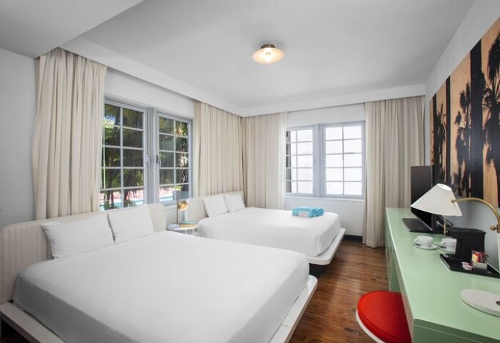 Axel Beach Miami gay-friendly hotel room with two beds, white linens, desk, and palm tree art. A modern, comfortable space for gay travelers.
