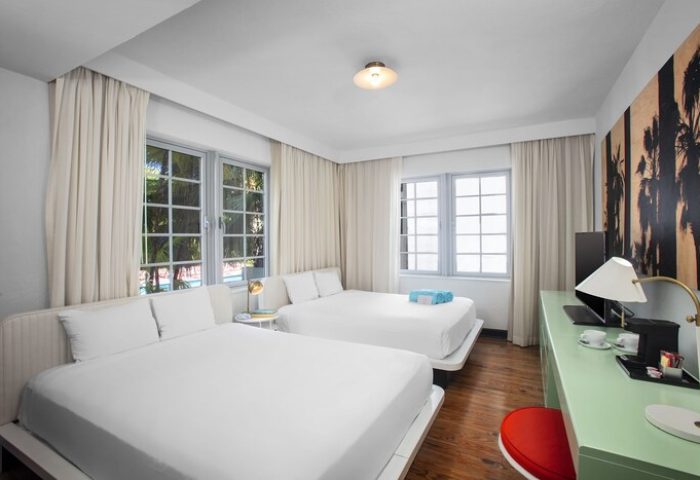 Axel Beach Miami gay-friendly hotel room with two beds, white linens, desk, and palm tree art. A modern, comfortable space for gay travelers.
