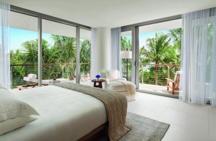 Miami Beach EDITION gay-friendly hotel room with balcony. Palm trees, ocean view. Luxury travel for gay men. Modern design, serene.