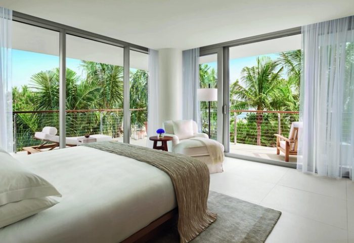 Miami Beach EDITION gay-friendly hotel room with balcony. Palm trees, ocean view. Luxury travel for gay men. Modern design, serene.