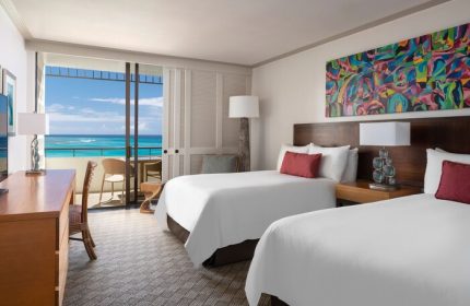 Royal Hawaiian, a Luxury Collection Resort, Waikiki gay-friendly hotel room with ocean view balcony. Two beds, colorful art, desk, chairs.