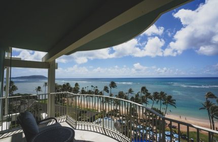 Balcony view at The Kahala Hotel and Resort, a gay-friendly hotel. Ocean, beach, and palm trees visible. Ideal for gay travel.
