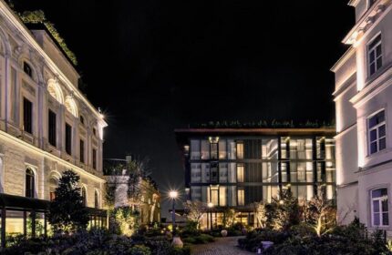 Night view of Soho House Istanbul, a gay-friendly hotel. The building's illuminated facade and lush greenery create an inviting ambiance.