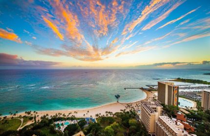 Hilton Hawaiian Village Waikiki Beach Resort view. Gay-friendly hotel with beach, ocean, palm trees, and colorful sunset. Ideal for gay travel.