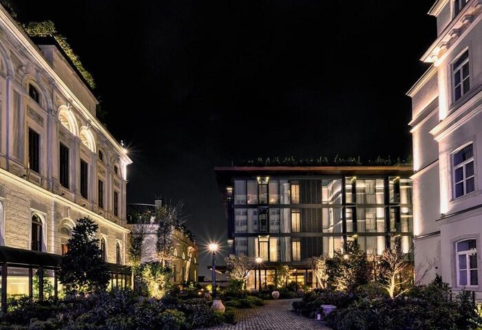 Night view of Soho House Istanbul, a gay-friendly hotel. The building's illuminated facade and lush greenery create an inviting ambiance.