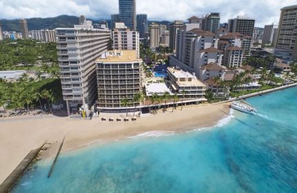 Outrigger Reef Waikiki Beach Resort view. Gay-friendly hotel on Waikiki Beach, Hawaii. Turquoise water, palm trees, and city skyline.