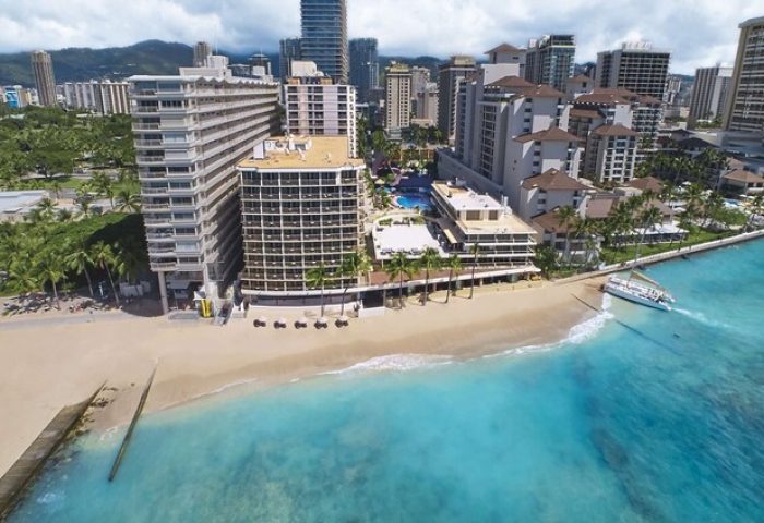 Outrigger Reef Waikiki Beach Resort view. Gay-friendly hotel on Waikiki Beach, Hawaii. Turquoise water, palm trees, and city skyline.