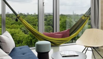 25Hours Bikini Berlin gay-friendly hotel room. Hammock, chair, and table. View of Berlin skyline. Modern design, comfortable space.