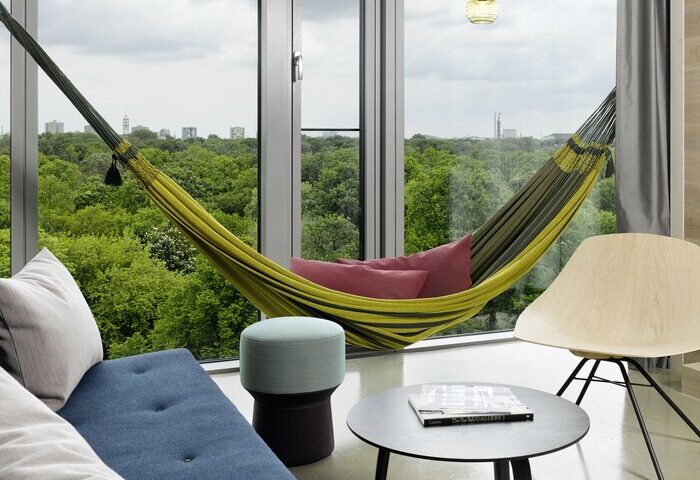 25Hours Bikini Berlin gay-friendly hotel room. Hammock, chair, and table. View of Berlin skyline. Modern design, comfortable space.