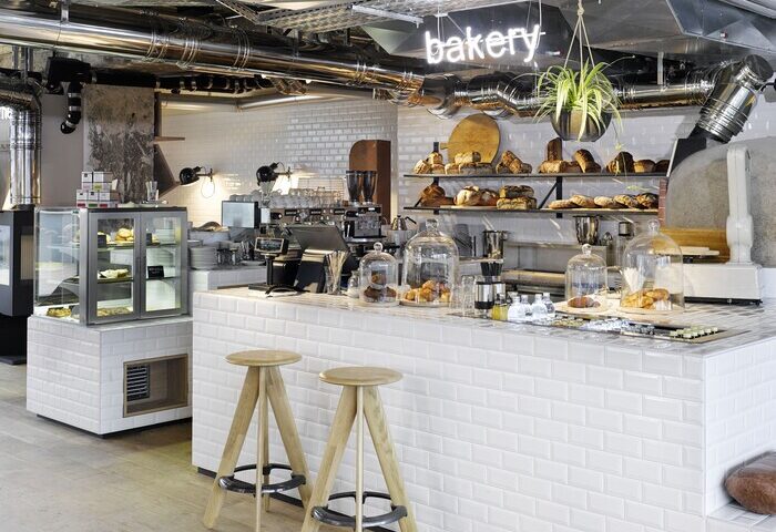 Bakery at 25Hours Bikini Berlin, a gay-friendly hotel. The stylish counter displays pastries and bread. A neon bakery sign hangs above.