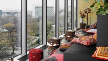 25Hours Bikini Berlin hotel lounge area with city view. Gay-friendly travel in Berlin, Germany. Stylish interior design with colorful pillows.