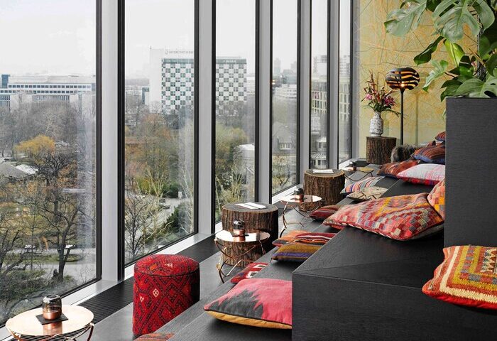 25Hours Bikini Berlin hotel lounge area with city view. Gay-friendly travel in Berlin, Germany. Stylish interior design with colorful pillows.