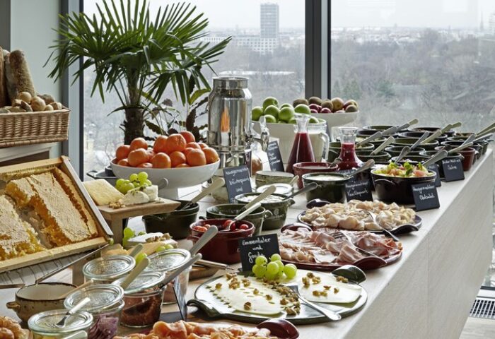 Breakfast buffet at 25Hours Bikini Berlin, a gay-friendly hotel. Features fresh fruit, cheese, meats, bread, and honeycomb. City view.