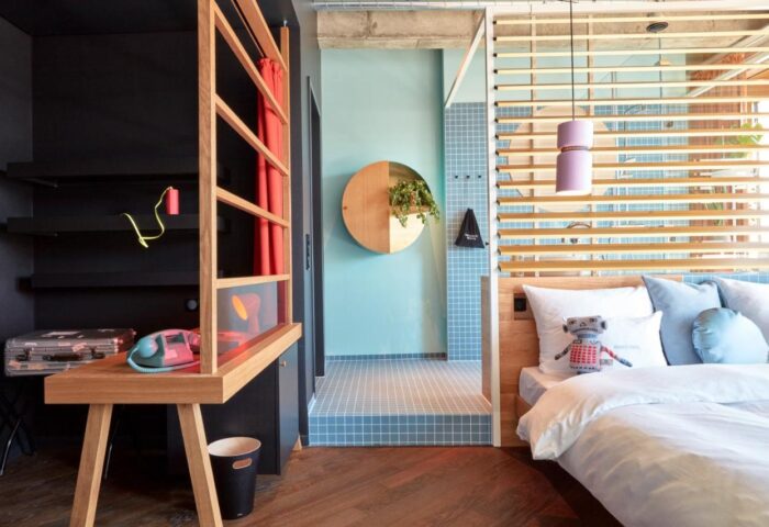 25hours Hotel The Circle interior. Gay-friendly hotel room with a bed, desk, and unique design elements. Modern, stylish decor.