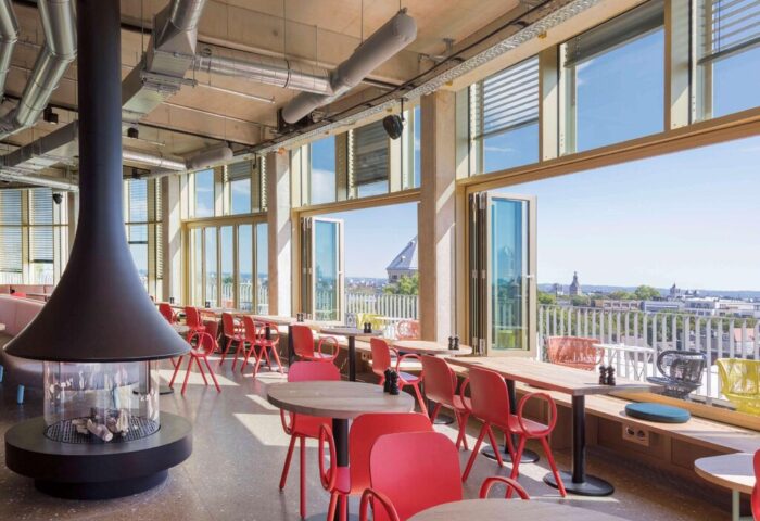 Interior of 25hours Hotel The Circle, a gay-friendly hotel. Red chairs, tables, and a modern fireplace. City view. Gay travel.