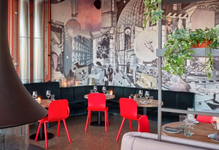 Interior of 25hours Hotel The Circle, a gay-friendly hotel. Red chairs, dark green banquette seating, and a mural create a unique atmosphere.