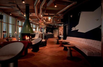 Interior of 25hours Hotel The Circle, a gay-friendly hotel. Features a fireplace, bar, and seating area. Modern design with exposed pipes.