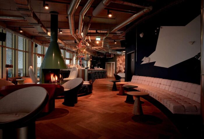 Interior of 25hours Hotel The Circle, a gay-friendly hotel. Features a fireplace, bar, and seating area. Modern design with exposed pipes.