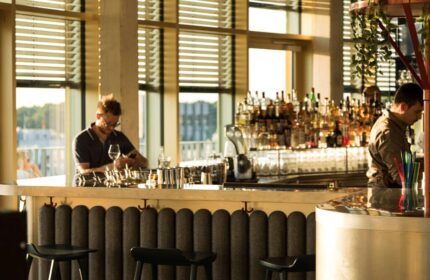Gay-friendly 25hours Hotel The Circle bar. Bartenders work behind a well-stocked bar with stools in a modern, stylish setting. Cologne, Germany.