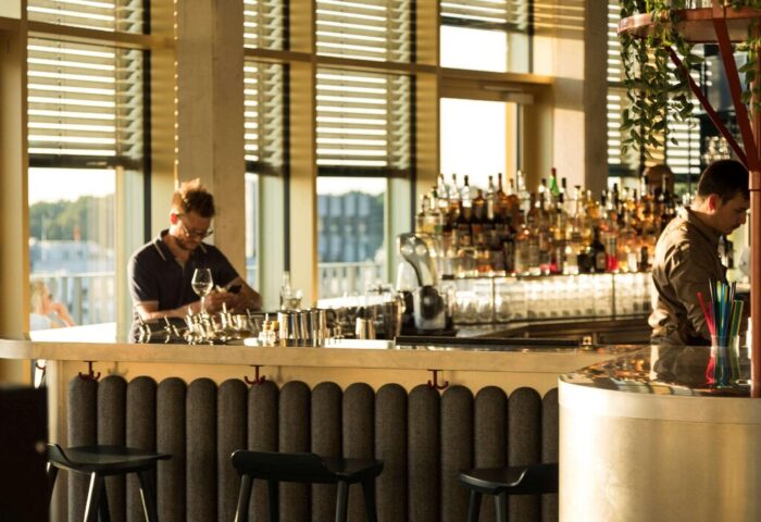 Gay-friendly 25hours Hotel The Circle bar. Bartenders work behind a well-stocked bar with stools in a modern, stylish setting. Cologne, Germany.