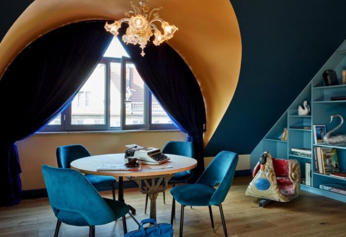 25hours Hotel The Royal Bavarian interior. Round table with typewriter, blue chairs, and stylish decor. Gay-friendly hotel.
