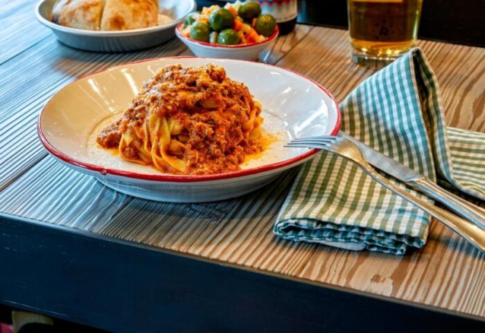 Dining at 25hours Hotel beim MuseumsQuartier. Pasta bolognese, beer, wine, olives, and bread on a wooden table. Gay-friendly hotel dining.