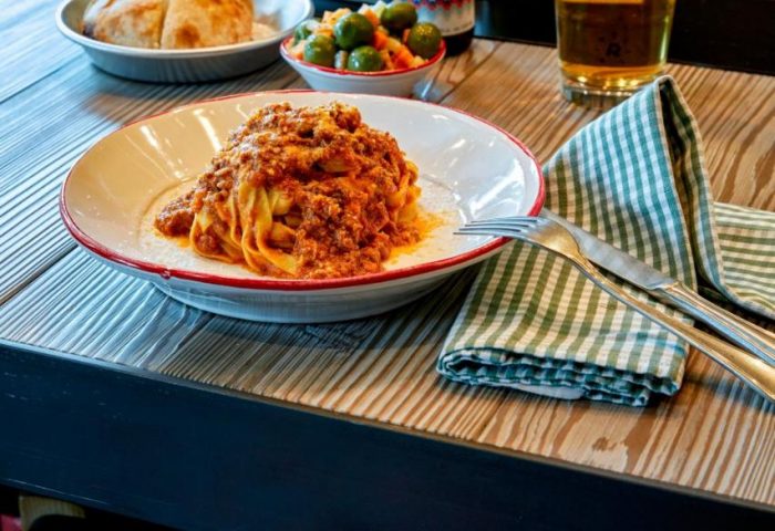Dining at 25hours Hotel beim MuseumsQuartier. Pasta bolognese, beer, wine, olives, and bread on a wooden table. Gay-friendly hotel dining.