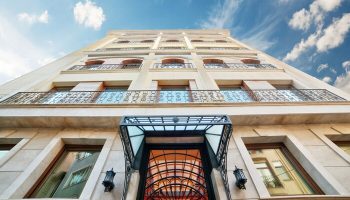 Facade of The Fox Hotel, a gay-friendly hotel. Low angle shot of the building's entrance and upper floors against a blue sky. Architecture.