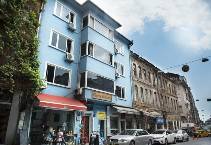 Cheers Midtown Hostel, a gay-friendly hotel. Blue building with a red awning over a cafe. Street view in Istanbul, Turkey.