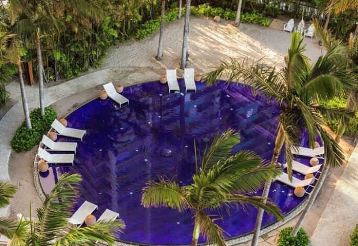 Aerial view of The Modern Honolulu's pool, a gay-friendly hotel. Palm trees and lounge chairs surround the vibrant blue water. Vacation awaits!