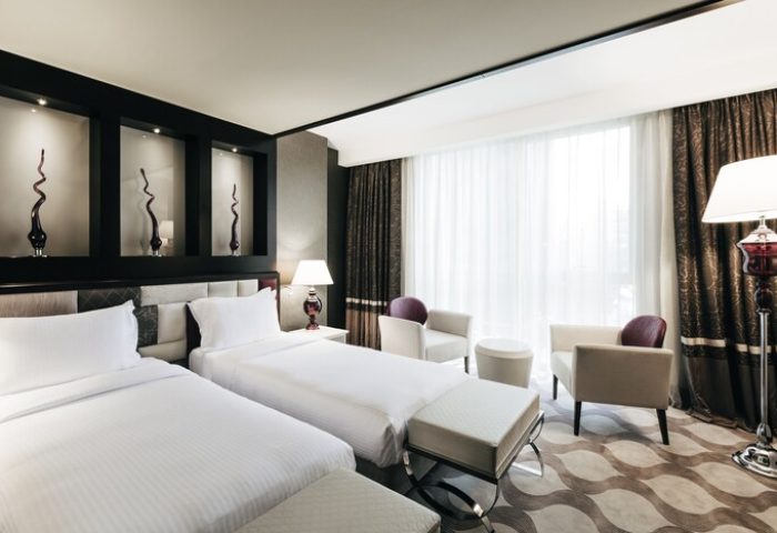 Elysium Taksim Hotel room with two beds, chairs, and lamps. Gay-friendly hotel with modern decor, ideal for gay travelers in Istanbul.